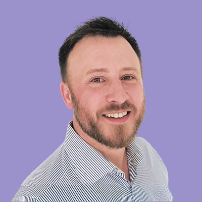 Smiling man with a beard and striped shirt against a purple background.