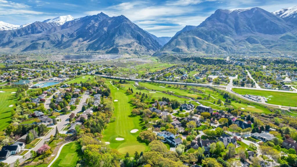 Aerial view of a city with a golf course and mountains in the background.
